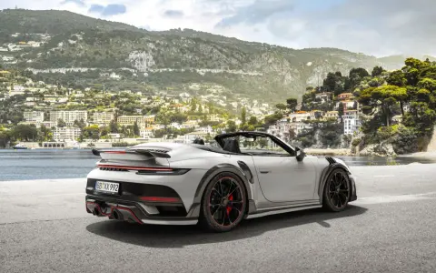 Ein weißer Techart GTstreet RS Cabriolet steht an einer Küstenstraße mit Blick auf eine malerische Stadt am Hang.