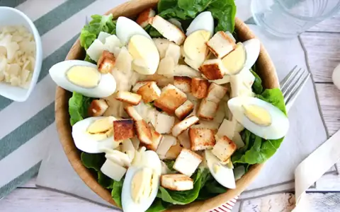 Salade César maison appétissante avec laitue, œufs durs, croûtons dorés et copeaux de parmesan. Parfait pour une recette facile et savoureuse.