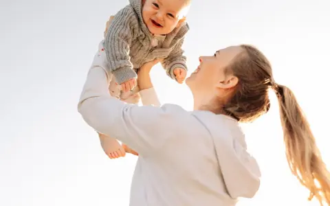 Mutter wirft ihr lachendes Baby in die Luft. Ein fröhlicher helikopter-mutter test im Freien.