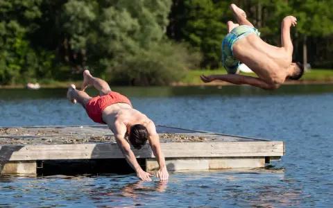 Zwei Männer springen vom Steg in den Sieglarer See. Einer macht einen Salto, der andere taucht gerade ins Wasser.