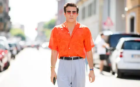 Hombre con camisa naranja estampada y pantalones grises, luciendo un elegante french tuck.