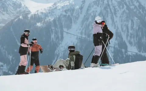 Grupa narciarzy i snowboardzistów odpoczywa na stoku, podziwiając majestatyczne góry Sierra Nevada.