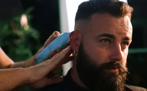 Un hombre con barba y aros en las orejas recibe un corte de pelo moderno, anticipando las tendencias de corte de pelo hombre 2026.