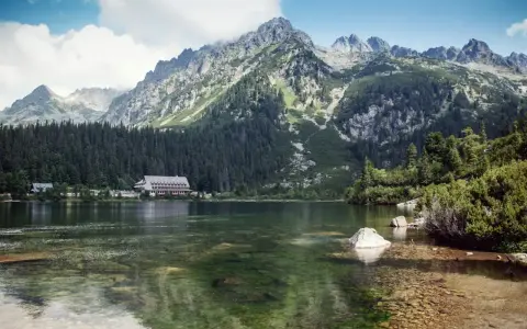 Malowniczy Popradzki Staw otoczony lasem i górami. Na brzegu hotel, w wodzie kamienie.