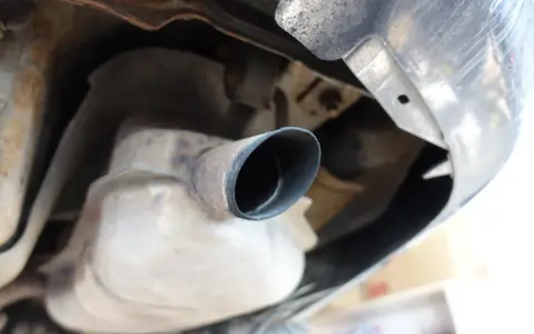 Widok od spodu samochodu na rurę wydechową z widocznymi osadami sadzy, co może wskazywać na pierwsze objawy zapchanego DPF.