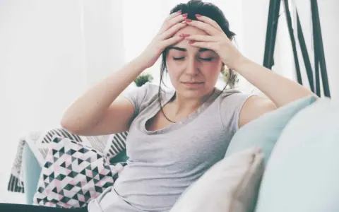Kobieta z rękami na skroniach, wyrażająca ból głowy, być może objaw psychosomatyki.
