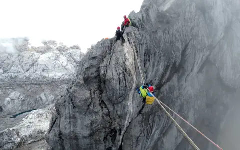 Wspinaczka na Piramidę Carstensza. Alpinista z plecakiem zjeżdża po linie, podczas gdy inni czekają na szczycie.