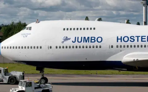 En person sitter på taket av ett jumbo stay. Flygplanet är vitt med blå detaljer och texten "JUMBO HOSTEL" syns tydligt.
