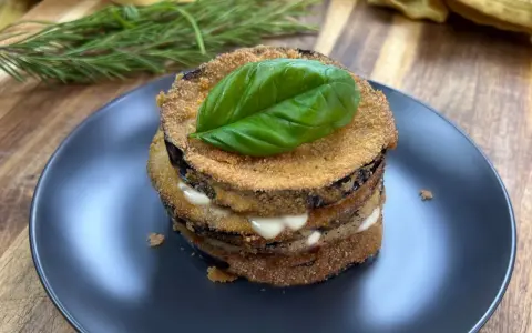 Deliziose cotolette di melanzane impilate, farcite con formaggio cremoso e guarnite con una foglia di basilico fresco.