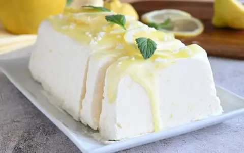 Un delizioso semifreddo al limone, guarnito con scorzette, menta e una glassa gialla brillante, pronto per essere gustato.