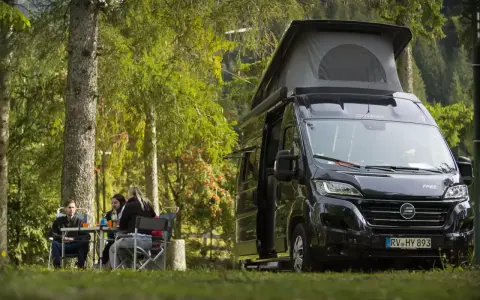 En solig dag med en clever sunny 540 husbil parkerad i skogen. Tre personer sitter vid ett bord och njuter av naturen.