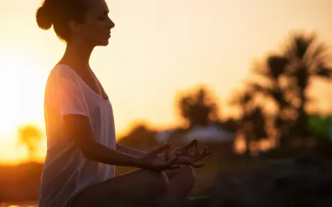 Frau meditiert im Sonnenuntergang. Ein kurzer 5-Minuten-Meditations-Text könnte hier perfekt passen, um diese friedliche Szene zu vertiefen.