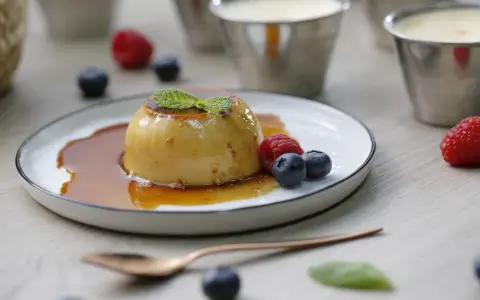Delicioso flan de queso con caramelo, adornado con menta y frutos rojos.