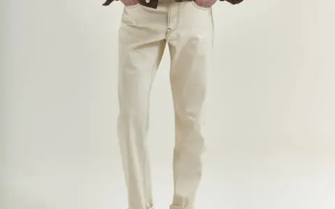 Uomo con giacca marrone e jeans chiari. La vestibilità è slim, non skinny, con risvolti alla caviglia.