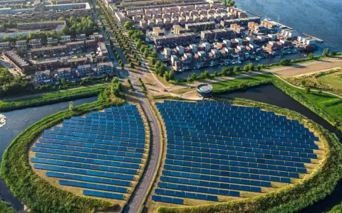 Un grande campo di pannelli solari, simbolo di rigenerazione urbana significato, circonda un quartiere residenziale con case moderne e canali.