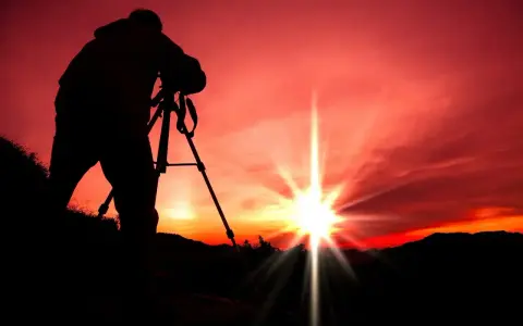 Silhouette d'un photographe sur trépied, capturant le soleil éclatant lors d'un coucher de soleil rougeoyant.