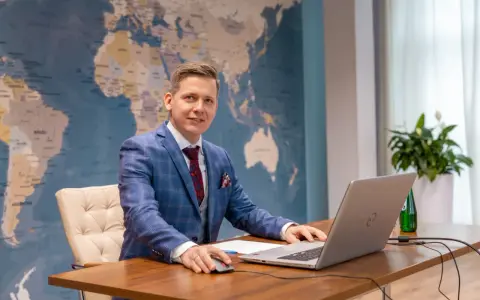 Mężczyzna w garniturze przy biurku z laptopem, na tle mapy świata. Tak wyglądają studia doktoranckie w dzisiejszych czasach – globalne spojrzenie i praca z technologią.