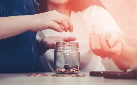 Dwie osoby wrzucają monety do słoika, oszczędzając na przyszłość. Zastanawiasz się, ile wynoszą alimenty na studenta?