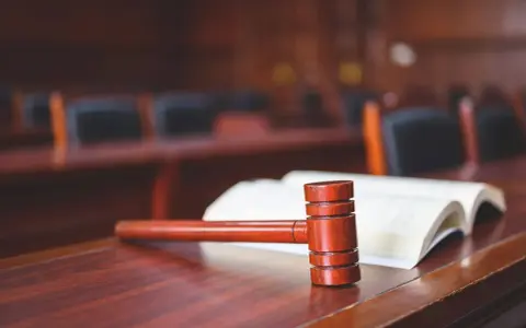 Młotek sędziowski i otwarta księga na drewnianym stole. Może to symbolizować formalne zrzeczenie się swojej części mieszkania w sądzie.