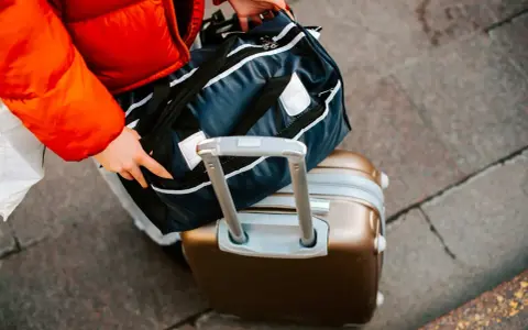 Osoba w czerwonej kurtce pakuje torbę podróżną na walizce. Zastanawiasz się, ile kosztuje bagaż rejestrowany?
