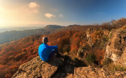 Ein Wanderer genießt den Ausblick auf die herbstliche Landschaft Norddeutschlands von einem Felsvorsprung.