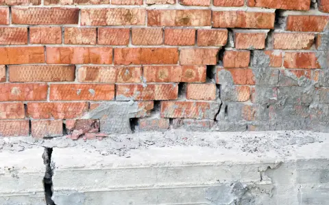 Pęknięta ceglana ściana i betonowy cokół, wskazujące na podbijanie fundamentów.