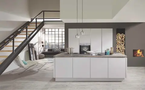 Cuisine moderne avec îlot central blanc. Le mur gris foncé contraste avec les meubles blancs et le bois de chauffage.