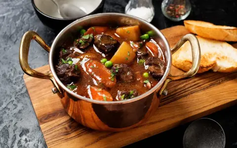 Herzhaftes Chili con Carne in Kupfertöpfchen, mit Kartoffeln, Karotten und Erbsen, serviert mit Baguette.