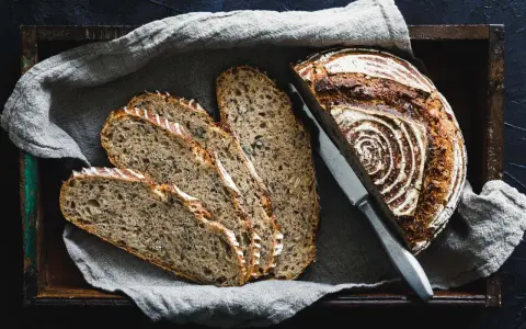 Ein rustikales Roggenbrot, in Scheiben geschnitten, liegt in einer Holzkiste auf Leinentuch. So vielseitig, was man aus Roggen machen kann!