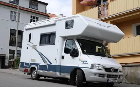 Biały kamper Fiat Ducato zaparkowany na ulicy. Zastanawiasz się, ile miejsc ma bus tego typu?