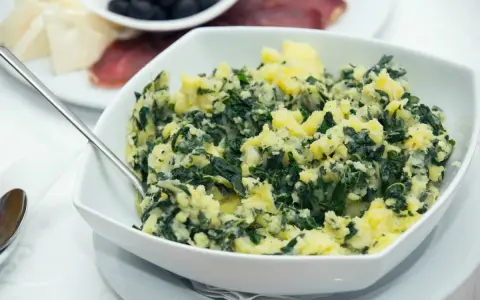 Un tazón blanco lleno de acelgas con patatas, un plato casero y reconfortante.