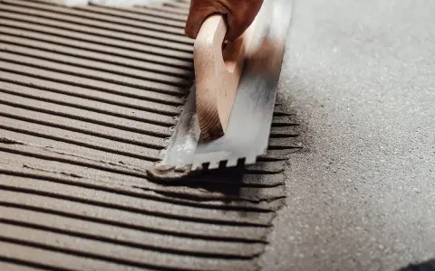 Application d'enduit pour carrelage avec une taloche crantée, assurant une épaisseur carrelage et colle uniforme pour une pose parfaite.