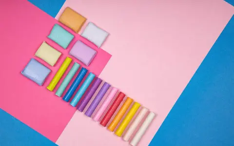 Kolorowe wałeczki i kostki modeliny, które twardnieją po wyschnięciu, ułożone na tle różowych i niebieskich kartek.