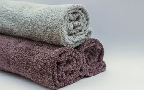 Trois serviettes de bain roulées, une grise et deux prune, prêtes à être cousues pour un projet de couture.
