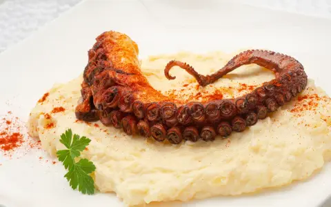 Delicioso pulpo a la plancha con puré cremoso, espolvoreado con pimentón y adornado con perejil fresco.