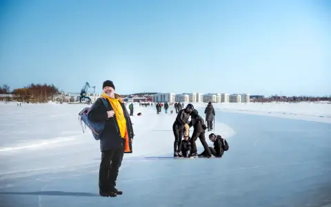 Glad man med ryggsäck njuter av en solig dag på isen i Luleå. Folk åker skridskor och promenerar i bakgrunden.