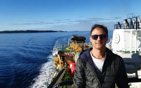 Uomo su nave, con mare e terra all'orizzonte. Un vero oceanografo significato, immerso nella sua ricerca.
