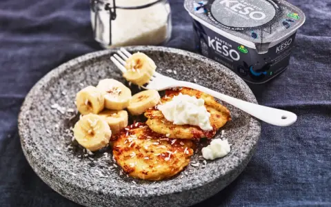 En tallrik med pannkakor toppade med keso och bananskivor. Perfekt för ett proteinrikt keso mellanmål.
