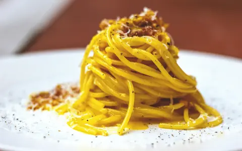 Un piatto di spaghetti alla carbonara fumante, guarnito con pecorino e pepe nero.