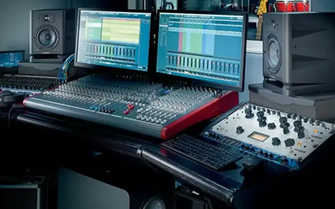 Station de mixage audio avec deux écrans, enceintes, casque et console de mixage.