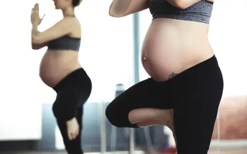 Ciężarna kobieta w czarnych legginsach i sportowym topie ćwiczy, odbijając się w lustrze. To może być jej sposób na aktywną zumbę w ciąży.