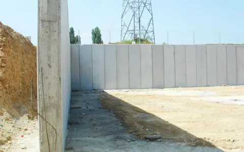 Construcción de muros de contención de hormigón prefabricados, con una torre de alta tensión al fondo.