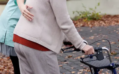 Opiekunka pomaga starszej osobie z chodzikiem. To przyszłość opieki, asystent osoby niepełnosprawnej 2026.