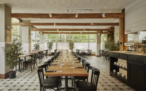 Elegancka sala restauracyjna z długimi stołami, idealna na degustację **primitivo kuchnia i wino**. Drewniane belki i duże okna tworzą przytulną atmosferę.