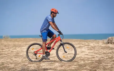 Mężczyzna w kasku jedzie na rowerze po plaży. Sprawdź, co obejmuje gwarancja roweru, by mieć pewność podczas każdej wyprawy.