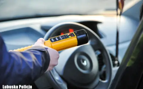 Policjant sprawdza, ile promili ma kierowca. Żółte światło na alkomacie sugeruje, że wynik jest poniżej dopuszczalnej normy.