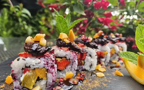 Roladki sushi z owocami, posypane cukrem pudrem i udekorowane miętą i pomarańczą.
