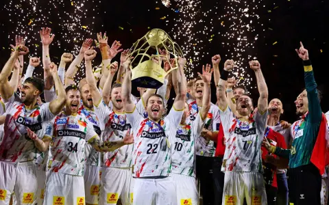 Drużyna świętuje zwycięstwo w finale piłki ręcznej, unosząc puchar. Konfetti i fajerwerki podkreślają radość.