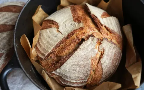 Ein frisch gebackenes Sauerteigbrot mit knuspriger Kruste liegt in einem Gusseisentopf. Perfekt für jedes Sauerteigbrot Rezept.