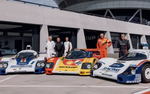 Fünf Rennfahrer stehen stolz neben ihren Porsche-Rennwagen der Gruppe C.